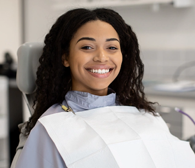 Smiling woman in dental bib at dentist office, seated in treatment chair.