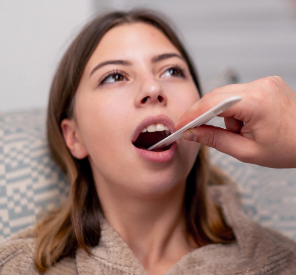 Woman receiving dental examination with tongue depressor in dentist's office.