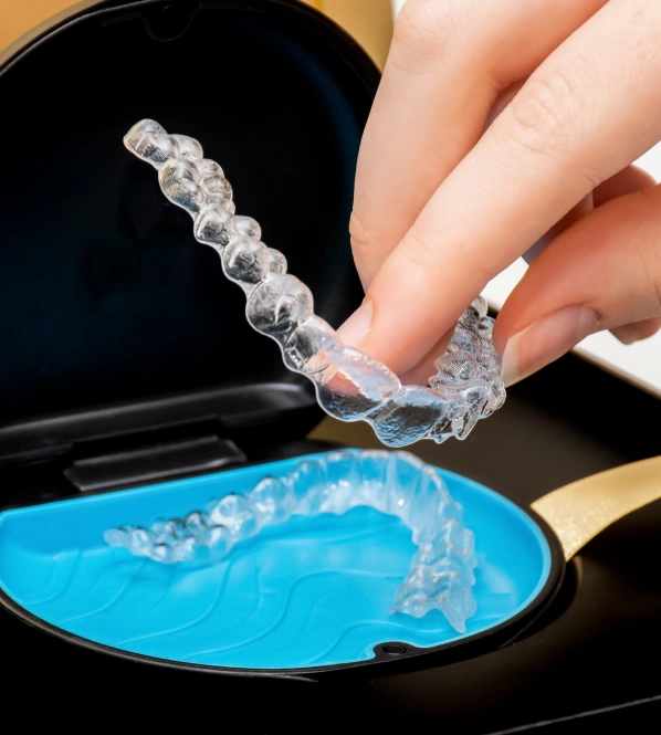 Person holding clear dental aligner tray over blue tray, demonstrating orthodontic treatment process.