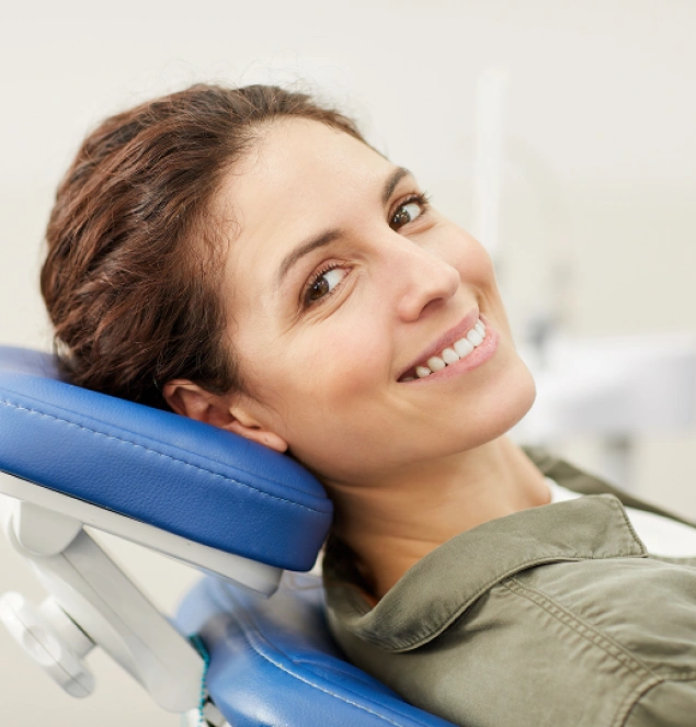 Woman smiling at dental office, resting head on blue headrest, wearing olive green shirt.