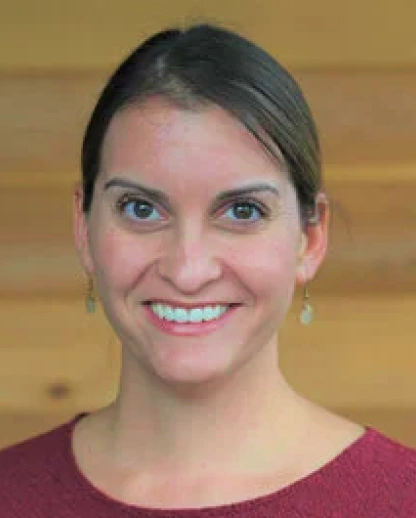 Professional headshot of smiling woman in maroon top against wooden background