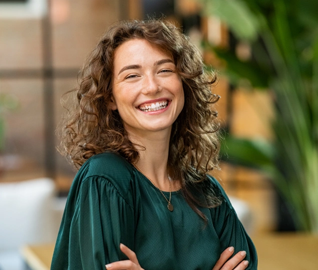 Smiling woman with curly hair wearing dark green shirt in modern dental office setting.