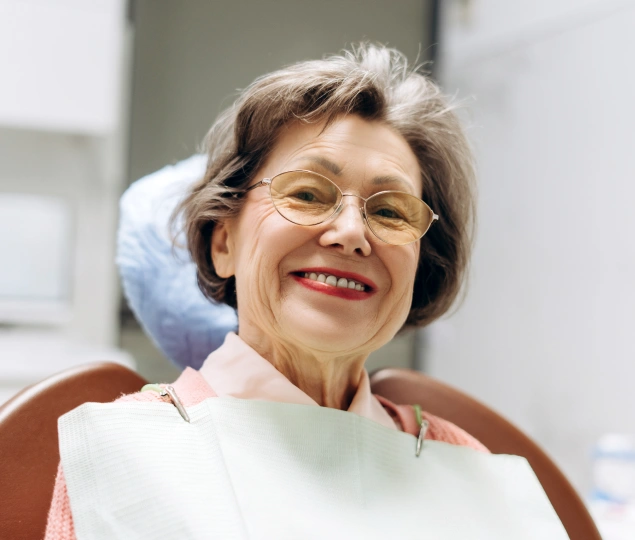 Smiling mature woman wearing glasses in dental office setting, appearing satisfied with dental care.