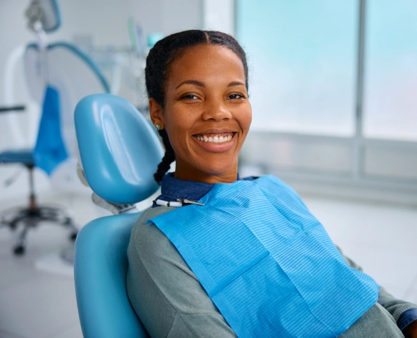 Smiling woman in dental chair wearing blue bib in modern bright dental office.