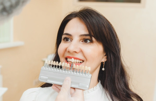 Woman smiling while holding teeth shade guide at dental office