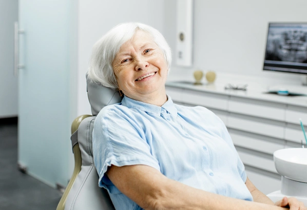 Senior woman smiling in dental office chair during examination or consultation.