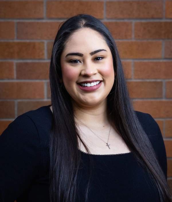 Professional headshot of smiling woman against brick wall background for dental practice.