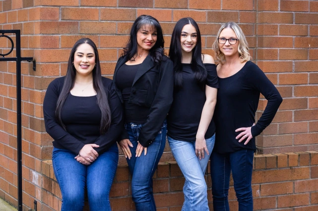 Four women dental staff members posing together against a brick wall background.