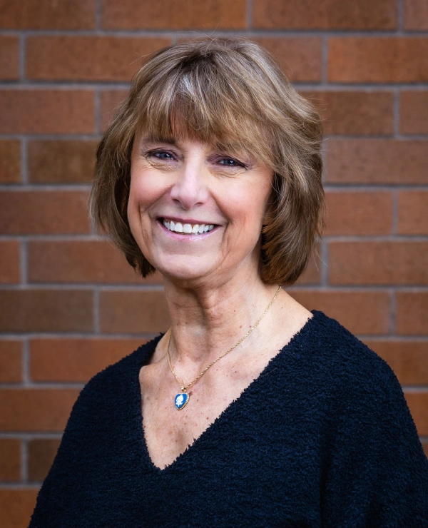 Professional headshot of smiling woman against brick wall background for dental practice.