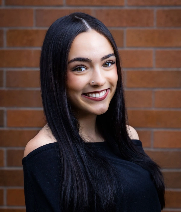 Young woman smiling at camera against brick wall backdrop for dental practice portrait.