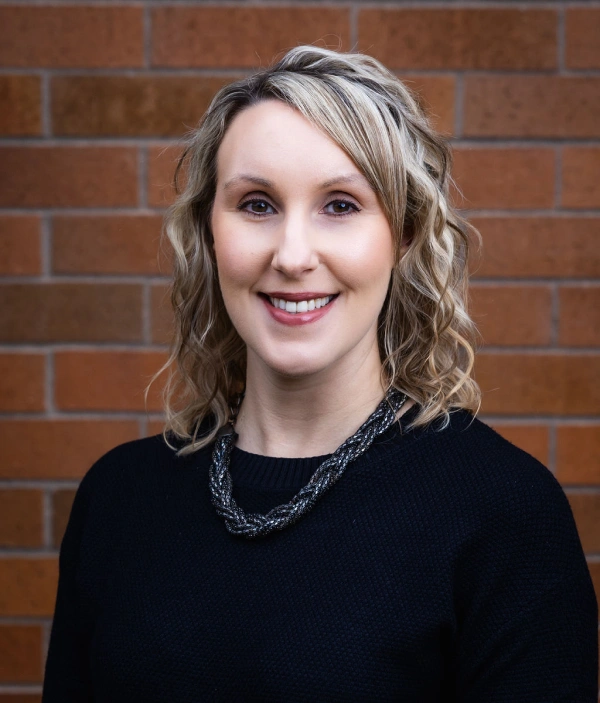 Professional headshot of woman smiling against red brick wall backdrop for dental practice.