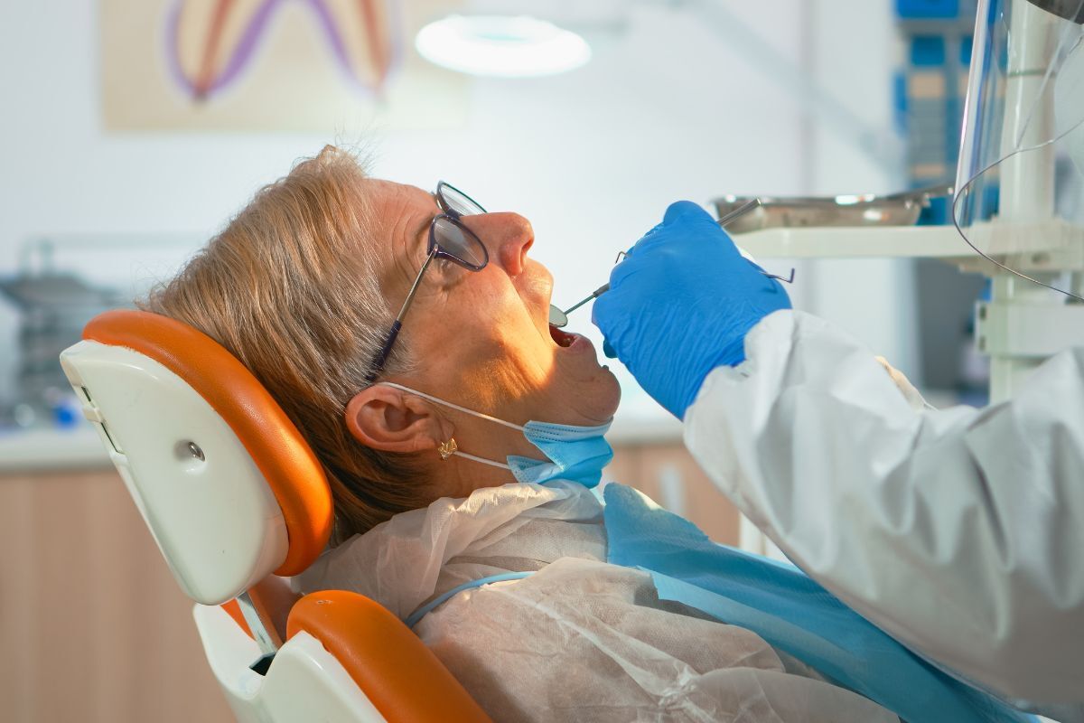 Senior woman receiving dental treatment in modern clinic chair with protective bib.